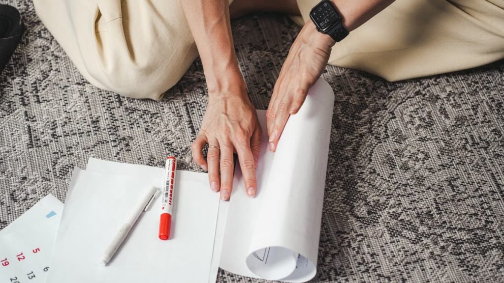 Close-up of hands rolling paper with a smartwatch, pen, and calendar on the floor.